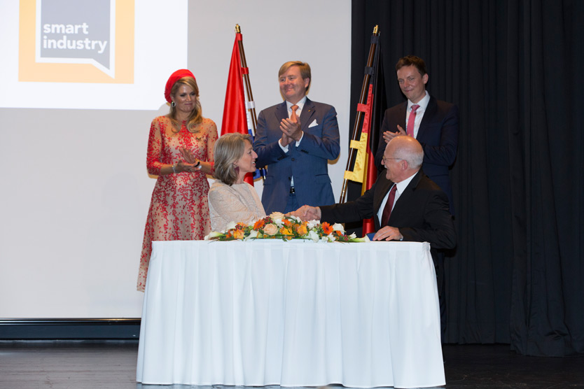 Thomas Hahn (Plattform Industrie 4.0) and Ineke Dezentje Hamming-Bluemink, (Smart Industry) at the signing of the agreement. In the background: the Dutch royal couple, Máxima and Willem-Alexander.